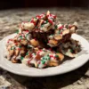 Delicious christmas crockpot candy recipe clusters with dark and white chocolate, almonds, and festive red and green sprinkles on a white plate.