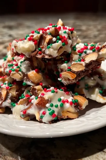 Delicious christmas crockpot candy recipe clusters with dark and white chocolate, almonds, and festive red and green sprinkles on a white plate.