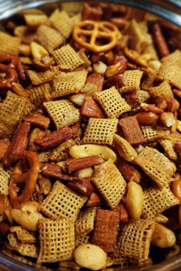 Overhead view of a delicious Christmas Chex Mix recipe in a polished metal bowl, featuring glazed Chex cereal, pretzels, nuts, and savory crisps, perfect for holiday snacking.