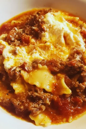 Close-up of a hearty lasagna soup recipe cooked in a crock pot, featuring pasta, rich meat sauce, and creamy ricotta in a white bowl.