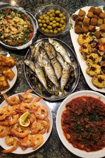 A vibrant Christmas seven fishes dinner recipe spread, featuring grilled fish, cooked shrimp, mussels, fried seafood, olives, and savory stews on a dark granite counter.