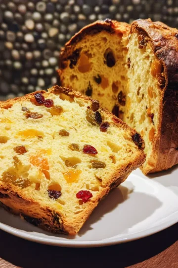 A delicious slice of homemade Christmas panettone recipe, rich with candied fruits, alongside the full loaf on a rustic wooden table.