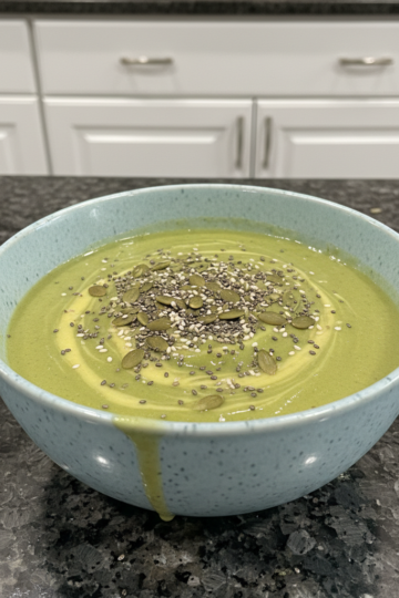 A creamy green avocado banana smoothie in a glass with a straw, garnished with a mint leaf, ready to drink.