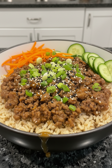A vibrant and nutritious Healthy Ground Beef Rice Bowl, topped with fresh avocado, cilantro, and a lime wedge, presented on a light wooden surface.