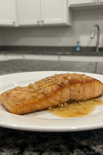 A perfectly seared honey garlic salmon fillet, garnished with fresh parsley and lemon, on a white plate.