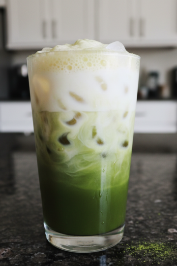 A vibrant green Iced Matcha Latte in a tall glass with ice and frothy milk, garnished with a straw.