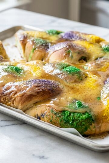 High-angle view of a king cake recipe on a white marble surface, glazed with brown butter and speckled with vanilla bean.