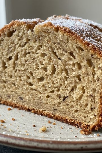 A golden-brown loaf of sourdough banana bread, sliced to reveal its moist, tender crumb, ready to enjoy.